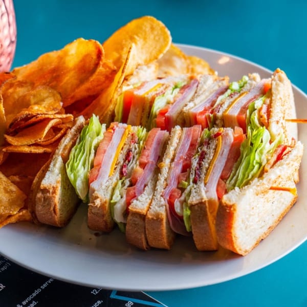 A club sandwich with chips on a white plate, showcasing Players Locker Room's sports-bar fare.