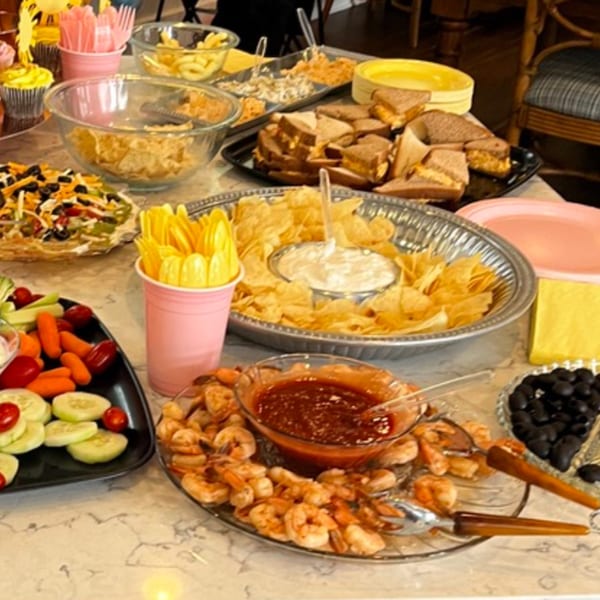A buffet table laden with various appetizers including shrimp cocktail, sandwiches, chips, and vegetables.