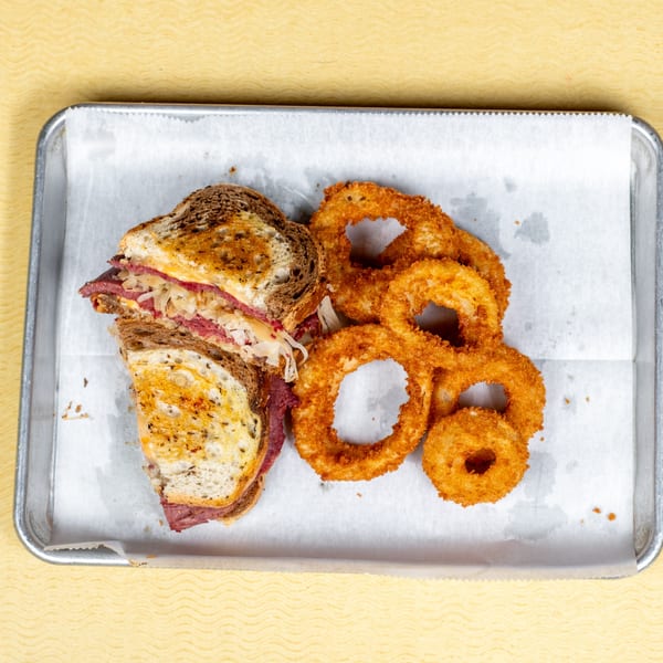 A Players Locker Room Reuben sandwich with crispy onion rings on a metal tray.