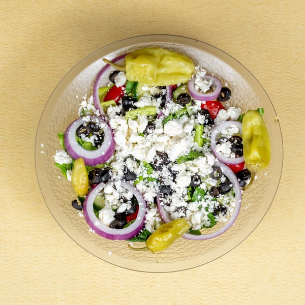 A fresh Greek salad with lettuce, red onions, olives, feta cheese, and pepperoncini.