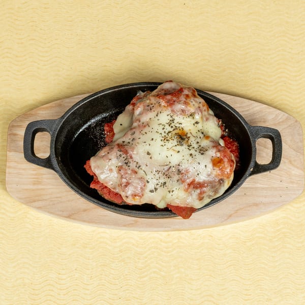 Melted cheese and tomato sauce dish in a black cast iron skillet on a wooden board.