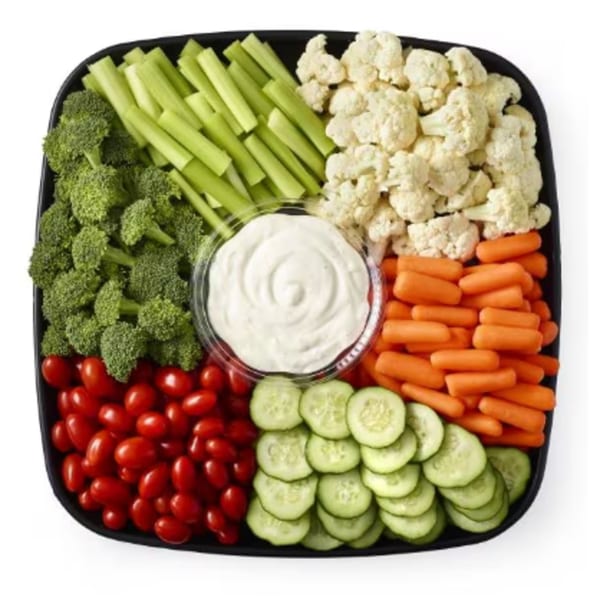 A black platter filled with broccoli, celery, cauliflower, baby carrots, cherry tomatoes, and cucumber slices around a dip.