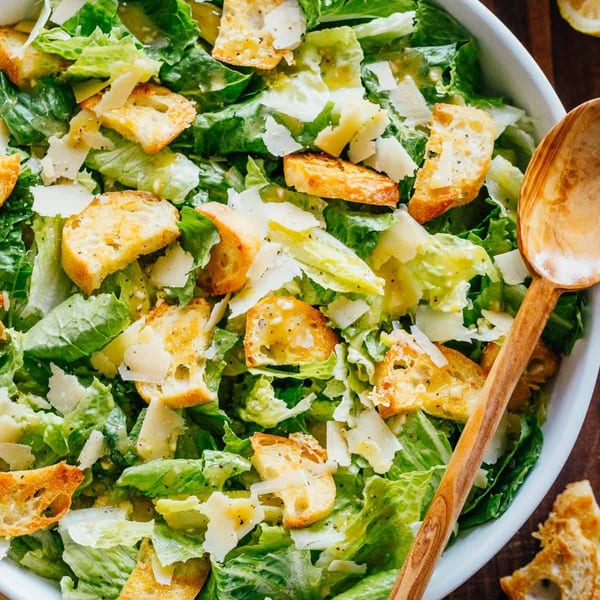 Close-up of a Caesar salad with romaine lettuce, croutons, and Parmesan cheese in a white bowl.
