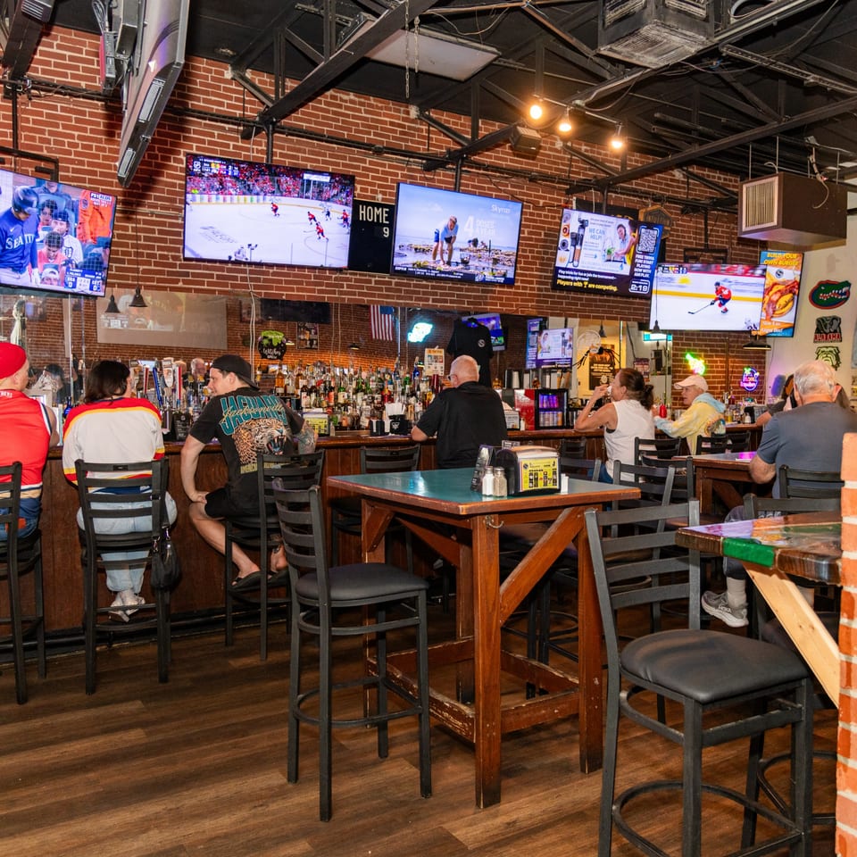 Patrons at the Players Locker Room sports bar, with multiple TVs showing sports and advertisements.